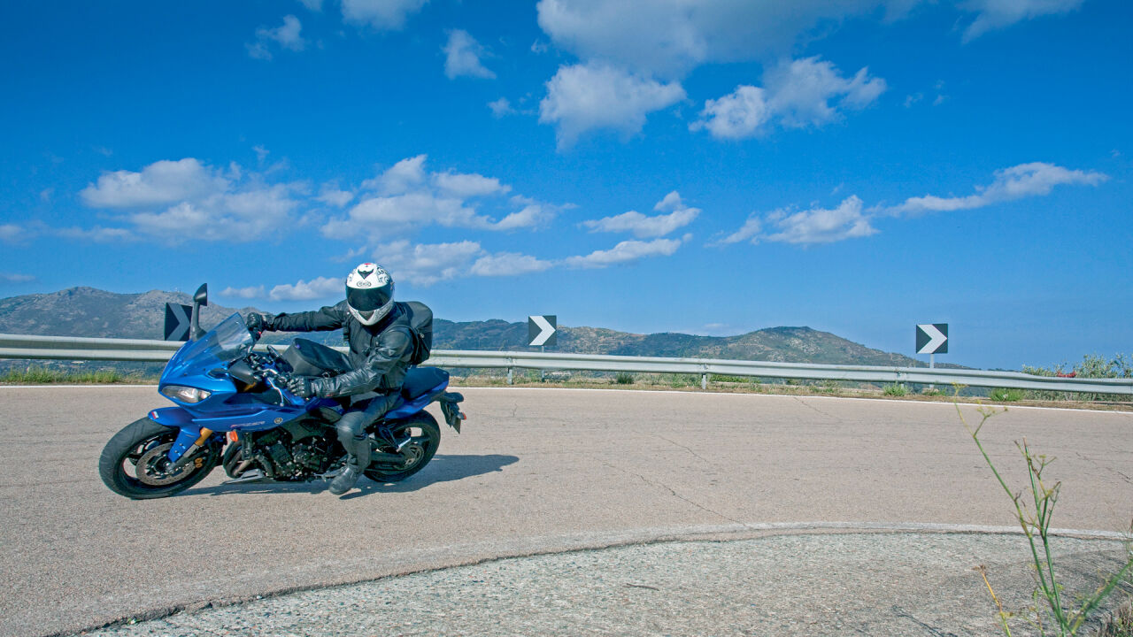 Motorrad in einer Kurve mit Leitplanke, Richtungspfeilen und Bergen im Hintergrund