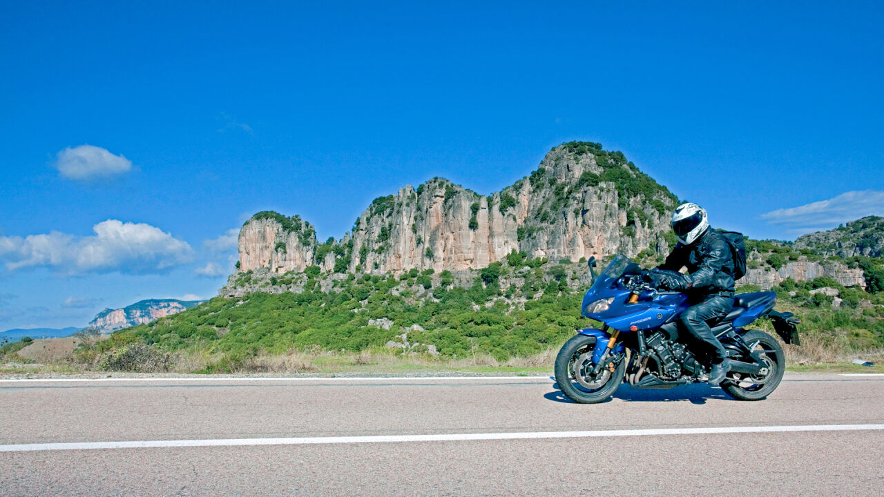 Motorrad auf einer Straße vor einer Kalksteinkette mit grünem Hang